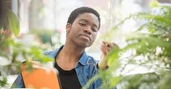 Female intern inspects a climate device in a greenhouse surrounded by plants.